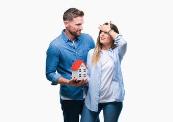 Young couple in love holding house over isolated background stressed with hand on head, shocked...