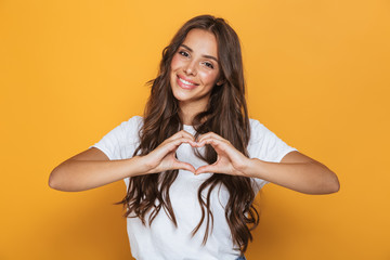 Image of charming woman 20s with long hair smiling and showing heart shape with fingers, isolated...