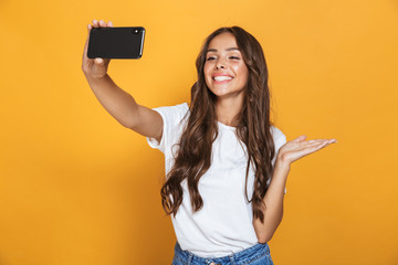 Portrait of positive woman 20s with long hair laughing while taking selfie photo on smartphone,...