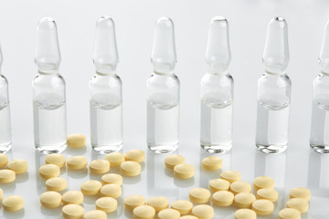 Ampoules with medicine and yellow tablets on white background