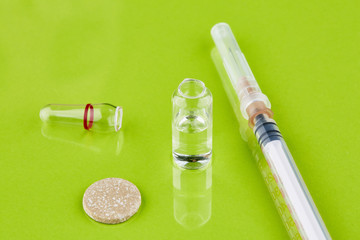 Ampoule with medicine and syringe on green background