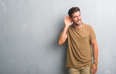 Handsome young man over grey grunge wall smiling with hand over ear listening an hearing to rumor...