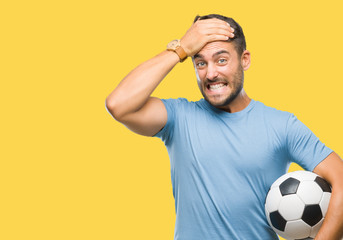 Young handsome man holding soccer football ball over isolated background stressed with hand on...