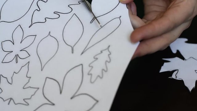 Cutting out of white paper leaves of trees with scissors on a printed template for applique and other creativity