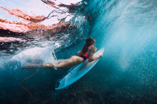 Surfer girl with surfboard dive underwater with under big wave.