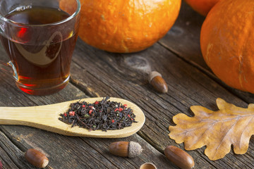 Autumn background on a wooden table with a pumpkins, a glass cup of tea and acorns