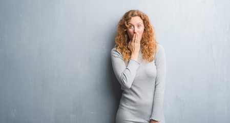 Young redhead woman over grey grunge wall cover mouth with hand shocked with shame for mistake,...