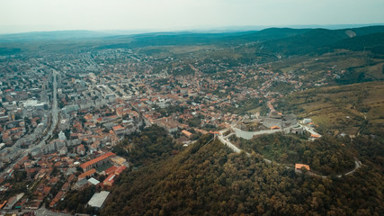 Aerial view of Deva Castle with the town in the background on a cloudy sky.