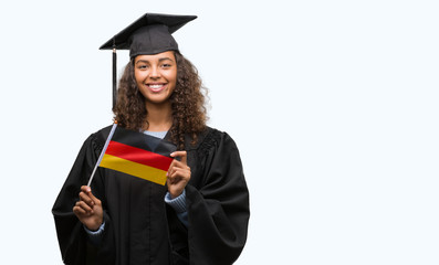 Young hispanic woman wearing graduation uniform holding flag of Germany with a happy face standing and smiling with a confident smile showing teeth