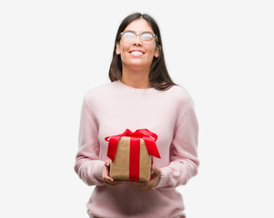 Young hispanic woman holding a gift with a happy face standing and smiling with a confident smile showing teeth