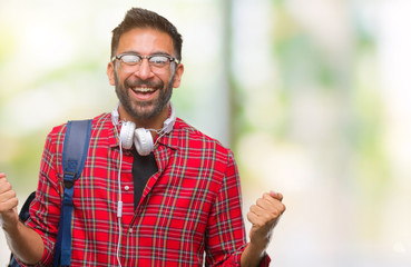 Adult hispanic student man wearing headphones and backpack over isolated background celebrating surprised and amazed for success with arms raised and open eyes. Winner concept.
