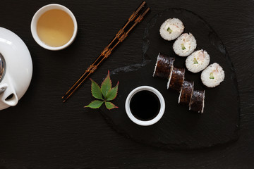 Japanese sushi with soy sauce on heart shape black  dish with chopsticks and traditional tea. Top view, close up on black concrete stone background
