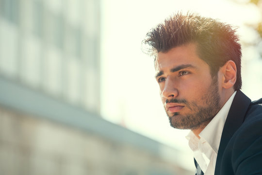 Young handsome man bearded and hairstyle. Hope attitude. He is outdoor with strong day sunlight from behind.