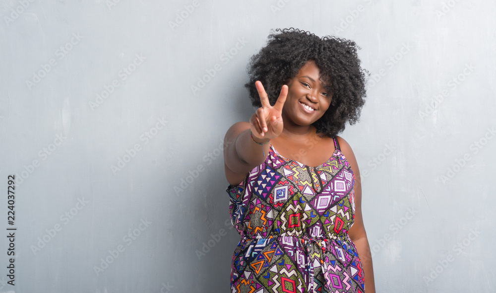 Wall mural young african american woman over grey grunge wall wearing colorful dress showing and pointing up wi