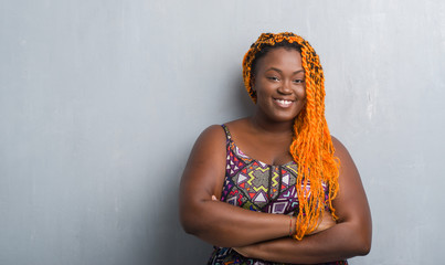 Young african american woman over grey grunge wall wearing orange braids happy face smiling with crossed arms looking at the camera. Positive person.