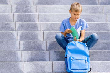 Boy reading book sitting on the stairs outdoors