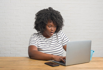 Young african american woman sitting on the table using computer laptop scared in shock with a surprise face, afraid and excited with fear expression