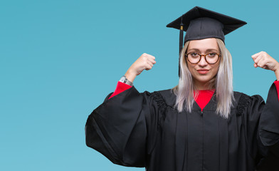 Young blonde woman wearing graduate uniform over isolated background showing arms muscles smiling proud. Fitness concept.