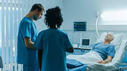 In the Hospital, Senior Man Sleeps in the Bed, Doctor and Nurse Have Discussion. Health Care Professionals at Work.