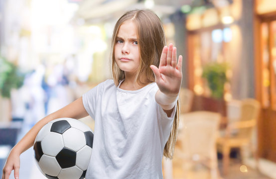 Young beautiful girl holding soccer football ball over isolated background with open hand doing stop sign with serious and confident expression, defense gesture