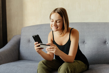 Happy attractive girl making online purchase via smartphone using debit credit card for payment,...