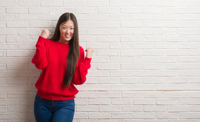 Obraz na płótnie Canvas Young Chinese woman over brick wall very happy and excited doing winner gesture with arms raised, smiling and screaming for success. Celebration concept.