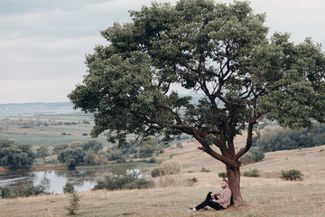 the man sits under a large tree of visas far away