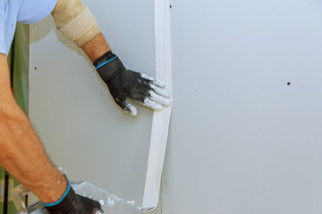 Worker in overalls plastering a wall with finishing putty using a putty knife. Repair work and...