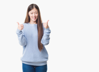 Young Chinese woman over isolated background success sign doing positive gesture with hand, thumbs up smiling and happy. Looking at the camera with cheerful expression, winner gesture.