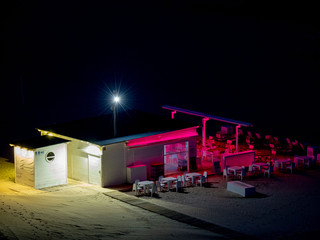 Empty beach bar with bar and chairs and tables lit with pink and white lights at night on the beach of Gandia, Spain