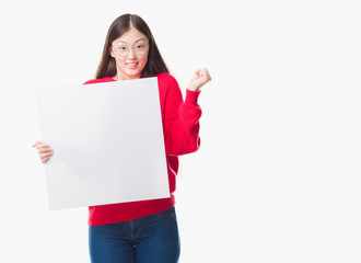 Young Chinese woman over isolated background holding blank banner screaming proud and celebrating victory and success very excited, cheering emotion