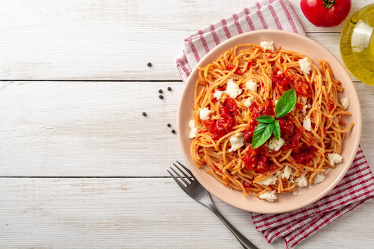 Spaghetti pasta with tomato sauce, mozzarella cheese and fresh basil in plate on white wooden background. Top view. Copy space.