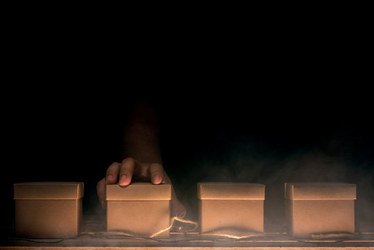 Hand Choosing A Box On Wooden Table In Mysterious Concept