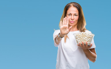 Middle age hispanic woman eating popcorn over isolated background with open hand doing stop sign with serious and confident expression, defense gesture