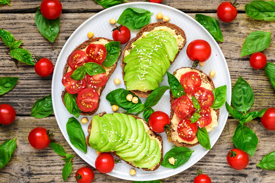 wholegrain bread avocado and tomatoes toasts with hummus, sesame and basil in a plate