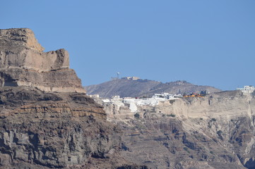 Fototapeta premium Wonderful Views Of The City Of Oia On Top Of A Mountain On The Island Of Santorini From High Sea. Architecture, Landscapes, Cruises, Travel. July 7, 2018. Pyrgos Island Santorini Greece.