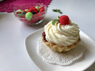 A cake basket with cream and berries and mint leaves. Nearby is a container with berries of different colors for decoration.