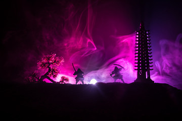 Samurai fighting concept. Silhouette of samurais in duel near tree and old temple. Picture with two samurais and sunset sky. Selective focus © zef art