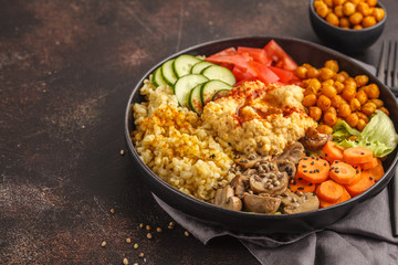 Buddha bowl with vegetables, mushrooms, bulgur, hummus and baked chickpeas. Dark background.
