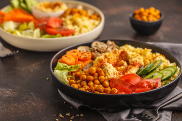 Buddha bowls with vegetables, mushrooms, bulgur, hummus and baked chickpeas. Dark background.