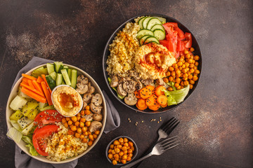 Buddha bowls with vegetables, mushrooms, bulgur, hummus and baked chickpeas. Dark background, top view.