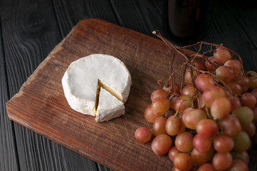 Bottles of wine on a black wooden background with grapes and cheese Camemberg