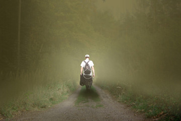 A young fisherman walks along a forest path into thick fog.