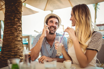 Happy couple sitting outdoors in cafe using phone