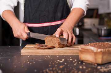 A man is cutting a whole-meal loaf of bread on wooden board.