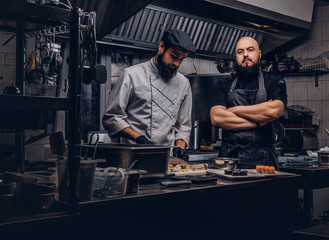 Fototapeta na wymiar Two brutal cooks dressed in uniforms preparing sushi in a kitchen.
