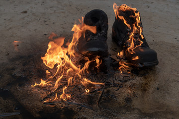 Black working boots made of thick pork skin burning in the fire. The concept of burning earth under...