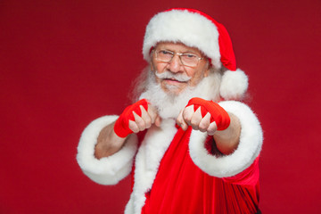 Christmas. Santa Claus with red bandages wound on his hands for boxing imitates kicks. Kickboxing, karate, boxing. Isolated on red background.