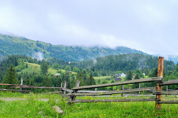 Fototapeta na wymiar wooden fence in the background of the village in the mountains of foggy. Ukraine Carpathians