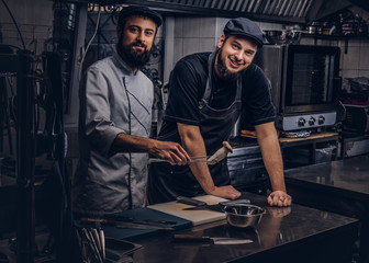 Smiling bearded cooks dressed in uniforms and hats having fun in kitchen.